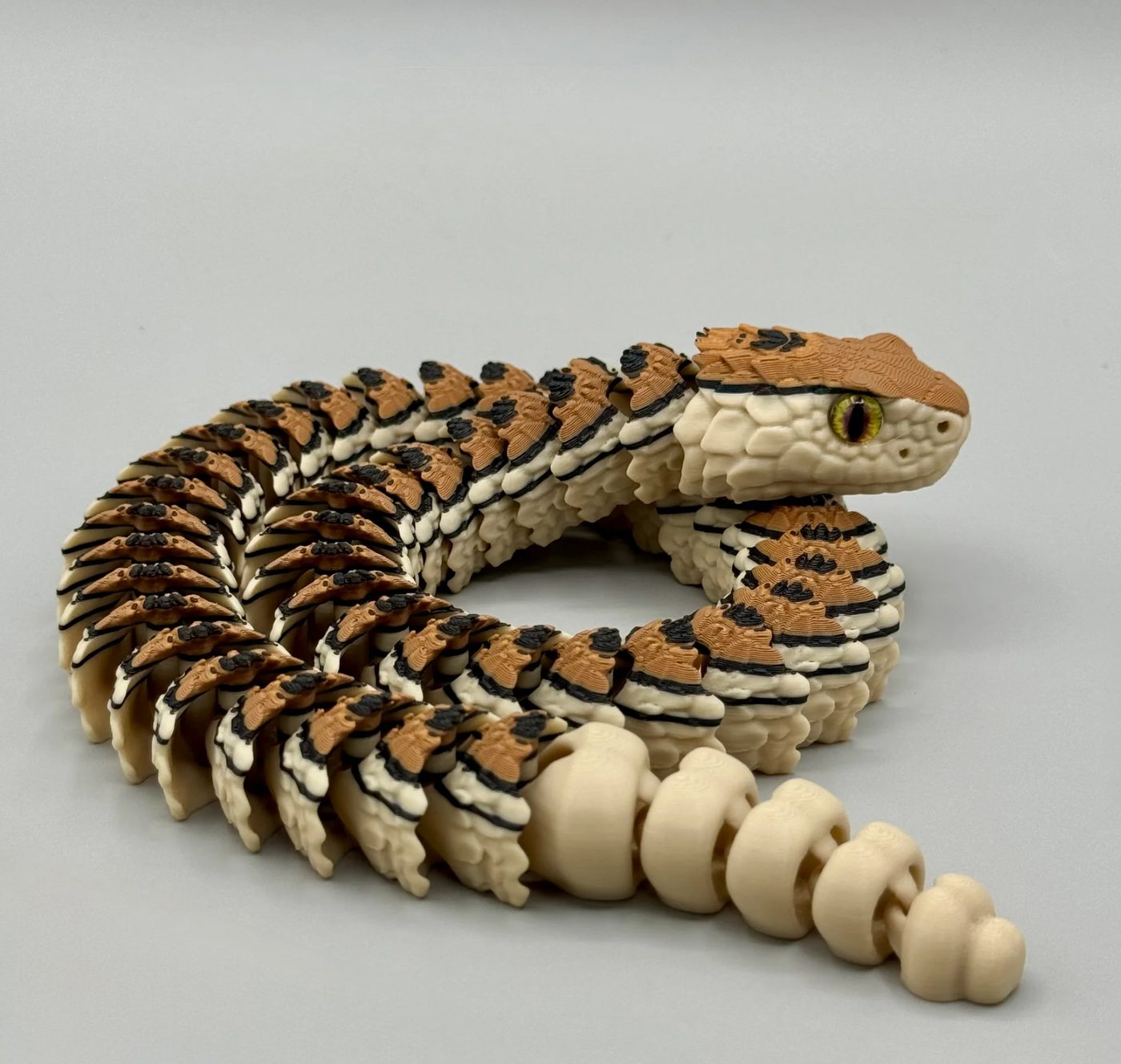 3D printed articulated rattlesnake coiled up, with layered tan and brown scales and a printed rattle tail