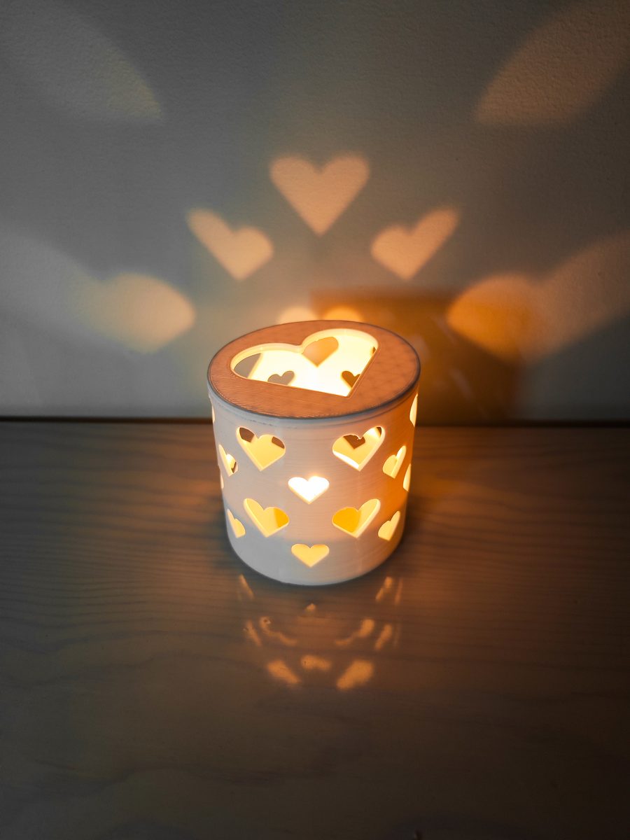 3D printed tealight holder with heart cutouts casting heart-shaped light patterns on the wall